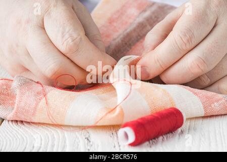 people, needlework, sewing and tailoring concept - tailor man with thread in needle stitching fabric. Hands sewing with a needle and thread. Fingers p Stock Photo