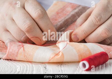 people, needlework, sewing and tailoring concept - tailor man with thread in needle stitching fabric. Hands sewing with a needle and thread. Fingers p Stock Photo