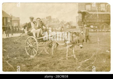 Early 1900's postcard of two happy smiling young working class men in a donkey and trap /cart, possibly racing (no. 137 next to wheel ), maybe at a fair or festival, or weekend activity, Wesleyan Home Missions Gospel Car in background, circa 1910, possibly Solihull, Birmingham, W. Midlands area, England, U.K. Stock Photo