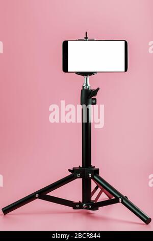 Mobile phone mounted on a tripod with a white display free for images and text, pink isolated background. Stock Photo