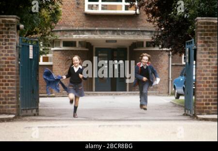 A young brother and sister running out of school at the end of the day, UK 1973 Stock Photo