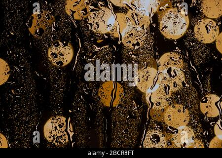 rain drops on night window and golden bokeh lights, drops background on night time Stock Photo