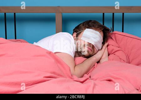 Young caucasian man wearing medical mask sleeping in bed. Studio shot Stock Photo