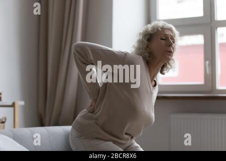 Elderly middle aged woman suffering from sudden sharp back pain. Stock Photo