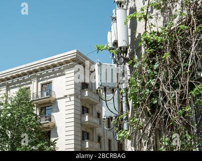 Multiple GSM LTE radio antenna communication tower covered with vine plant and renovated soviet apartment buildings in background central Baku, Azerbaijan Stock Photo