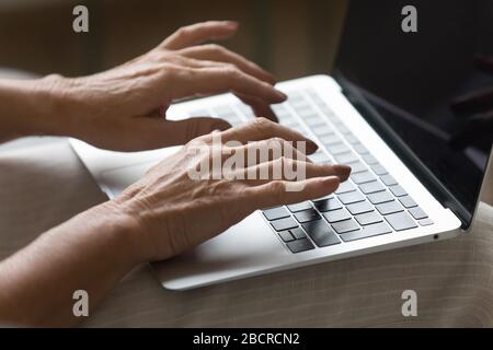 Wrinkled female hands typing message on laptop keyboard. Stock Photo