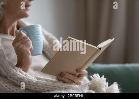 Smiling elderly senior woman drinking tea, reading paper book. Stock Photo