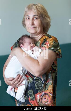 Mature Caucasian woman portrait carrying baby in arms, month old infant sleeping, female looking at camera Stock Photo