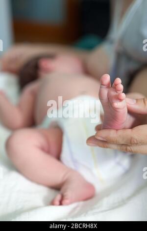 Newborn infant barefoot leg in women hand, mother breastfeeding baby lying in bed, close-up view Stock Photo