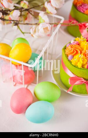 Spring Easter festive table. Small green cakes with butter cream flowers and colorful eggs on the background Stock Photo