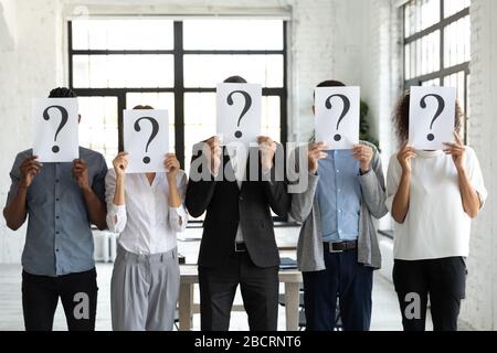 Business people hiding faces behind papers sheets with question marks. Stock Photo