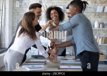 Smiling diverse employees stack fists at corporate meeting, celebrating success. Stock Photo
