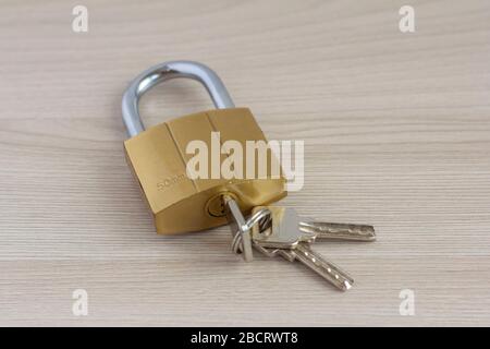 Closed padlock with keys in the keyhole on a light wooden background. Stock Photo