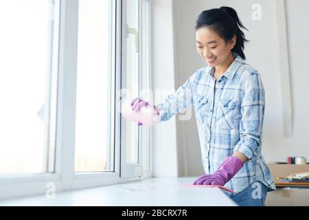 Waist up portrait of Smiling woman washing windows during Spring cleaning, focus on female hands wearing pink gloves, copy space Stock Photo