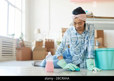 Full length portrait of happy Asian woman cleaning floor in new house or apartment after moving in, copy space Stock Photo
