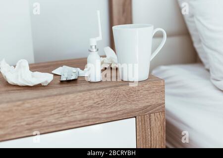 Medicines, pills, nose drops, tissues and hot drink cup on bedside table in modern apartments. Being sick, unwell, flu, illness symptoms. Coronavirus Stock Photo