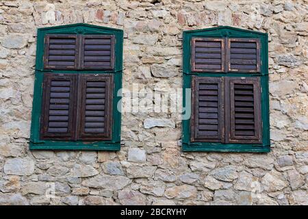two windows on old house with stone exterior walls; wooden shutters closed Stock Photo
