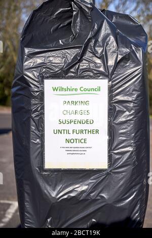 Public car park ticket machine covered with bin bag and a poster advising parking charges suspended during Coronavirus emergency Stock Photo