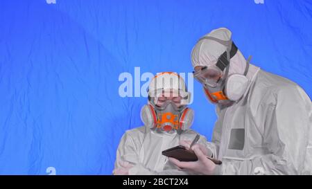 Scientist virologist in respirator makes write in an tablet computer with stylus. Man and woman wearing protective medical mask. Chroma key blue. Stock Photo
