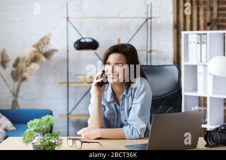 Working from home.Communication online with colleagues and freelancers.Portrait of young female freelancer talking on smartphone and smiling. Concept Stock Photo