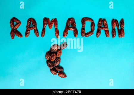 'Ramadan' word made of delicious date fruits on blue background. Ramadan kareem with arabic dates fruit in shape of crescent moon. Stock Photo