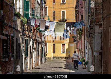 A man walks along Corte Calle Colonne a small narrow courtyard in Venice,Italy with washing hanging out to dry on a line strung between houses ,Venice Stock Photo