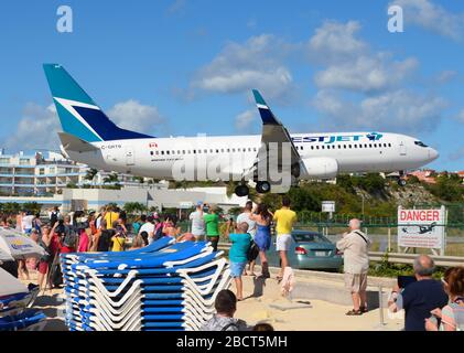 WestJet Airlines Boeing 737 passing over Maho Beach in St. Maarten. Low approach over the beach. Extreme airport. Aircraft registered as C-GRTB. Stock Photo