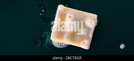 Bar of soap with foam bubbles on black background panoramic banner texture. Top view. Stock Photo
