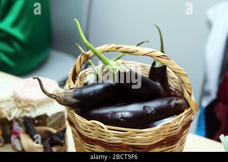 eggplant in a wicker basket on wooden table with blurred background . purple eggplant with stem in rattan basket Stock Photo
