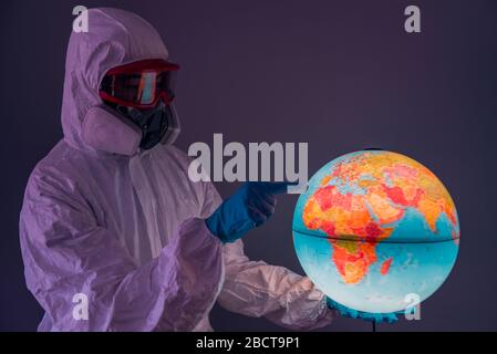 Concept: world viral crisis. Woman wearing lab coat, nitrile gloves, safety glasses, face mask and NBC suit for covid-19 coronavirus, at home confinement. Stock Photo