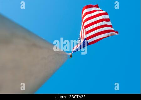 image looking up stainless steel flagpole at american flag waving in breeze agains clear blue sky Stock Photo