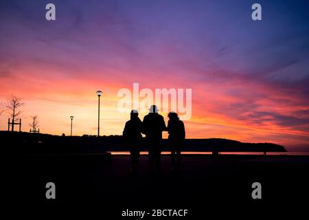 Older man with two women silhouette holding hands and walking in the sunset. Stock Photo