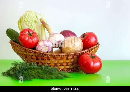 The wicker basket is on the table with tomatoes, garlic, cucumber, potatoes, cabbage, onions and a bunch of dill on the green table. Vegetarian Vegeta Stock Photo