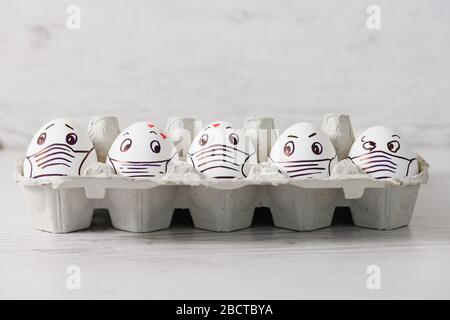 Five white eggs in tray close up with drawn emotional eyes, hearts and medical mask as canceled Easter holiday during april coronavirus quarantine Stock Photo