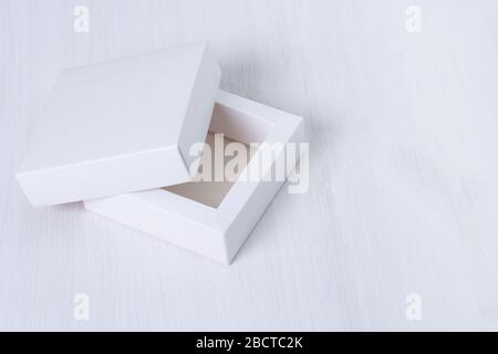 Open empty white gift box with a lid on isolated wooden background. Side view, square box. Elegant eco-friendly mockup. Isolated cardboard box with Stock Photo
