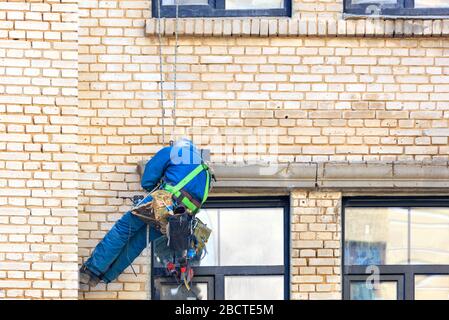 Builder climber hanging on safety ropes on the wall of an old building with a set of different tools behind. Stock Photo