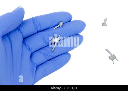 dental pins, posts and cast posts in the dentist's hand. in a glove there is a cast pin on a white background. restoration of teeth with great deterio Stock Photo