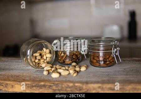 Pistachios scattered on the white vintage table from a jar and with other nuts on background. Pistachio is a healthy vegetarian protein nutritious Stock Photo