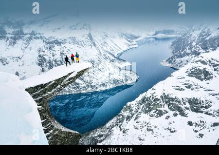 Tree young boys standing on famous Trolltunga rock in Norway and looking to the mountains Stock Photo