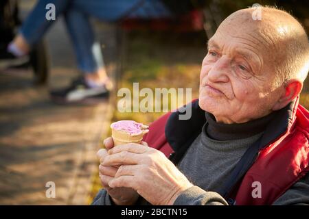 Eighty-year-old man walks in a public park, eats ice cream in a waffle cup Stock Photo