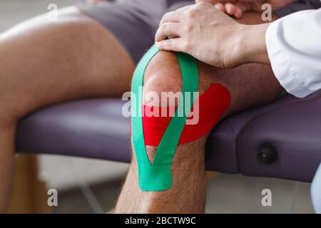 Kinesiology taping.Physical therapist applying kinesiology tape to patient knee.Therapist treating injured knee of young athlete.Post traumatic Stock Photo