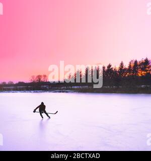 Hockey player silhouette on ice. Sunset sky in background. Stock Photo