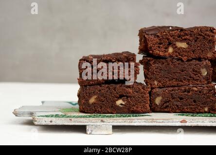 stack of square baked pieces of brownie chocolate cake with walnuts, on a wooden board, close up Stock Photo