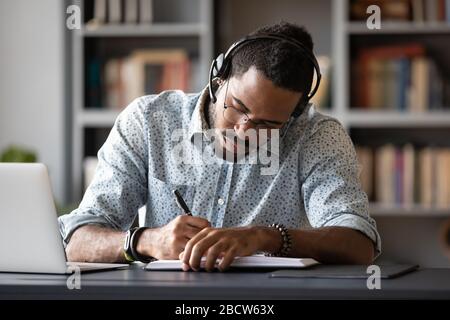 Focused biracial man in headphones make notes studying Stock Photo