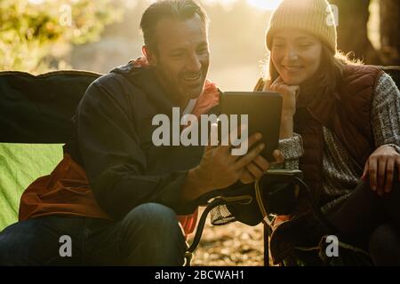 Smiling man and woman resting next to the tent and using digital tablet. Campers with digital tablet. Stock Photo
