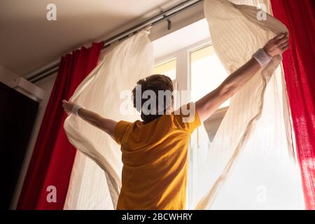 Caucasian man opening curtains on window to the morning light Stock Photo