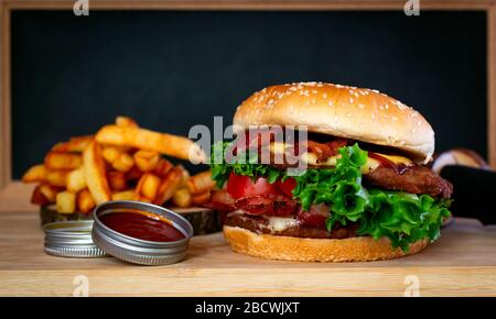 Delicious fresh homemade burger with lettuce, cheese, onion and tomato on rustic dark background wood plank Stock Photo