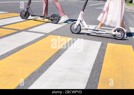 Young woman legs and man legs walking with scooters on cross road Stock Photo