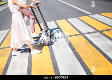 Young woman legs in pink tulle skirt and man legs walking with scooters on cross road Stock Photo
