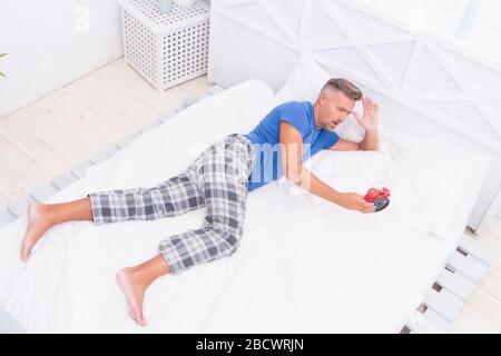 time is gone. stressful man wake up turn off the alarm clock. Time to wakeup. Tired unhappy man in bed. man suffering from headache. terrible loud noise. insomnia and sleep disorder. daily routine. Stock Photo